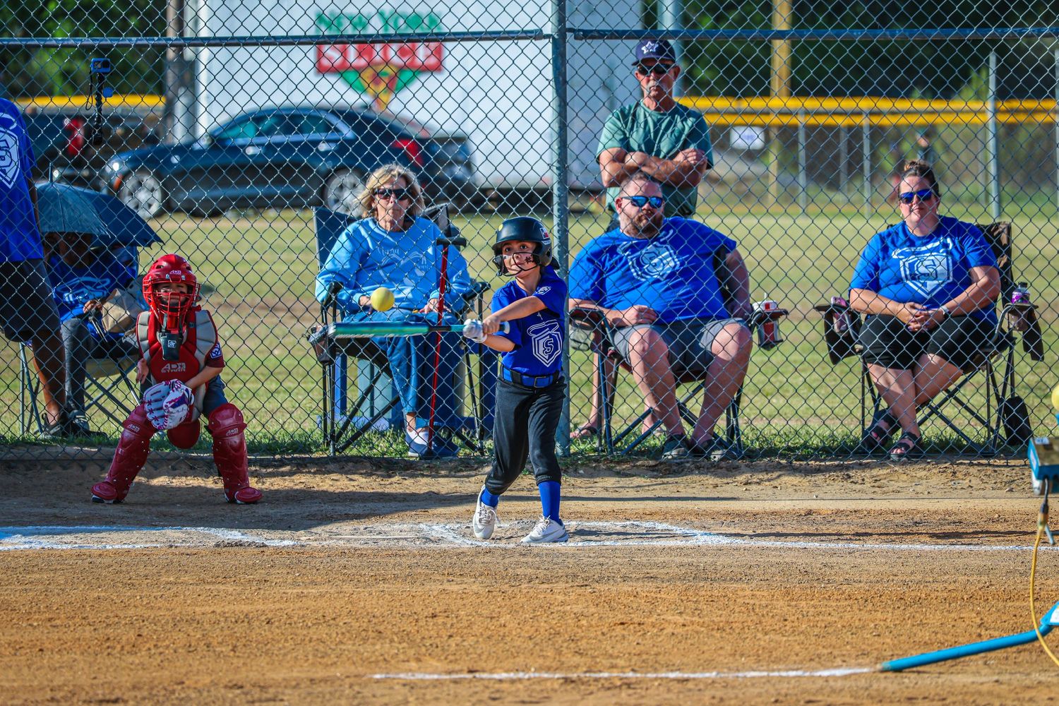 Young girl in blue uniform batting at home plate during a youth softball game.
