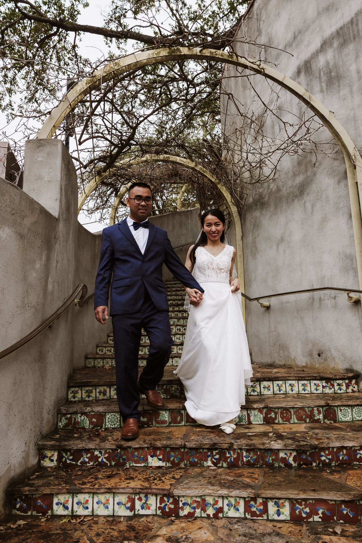 Couple sits together on decorative tiled wall with arched architecture in romantic outdoor setting.