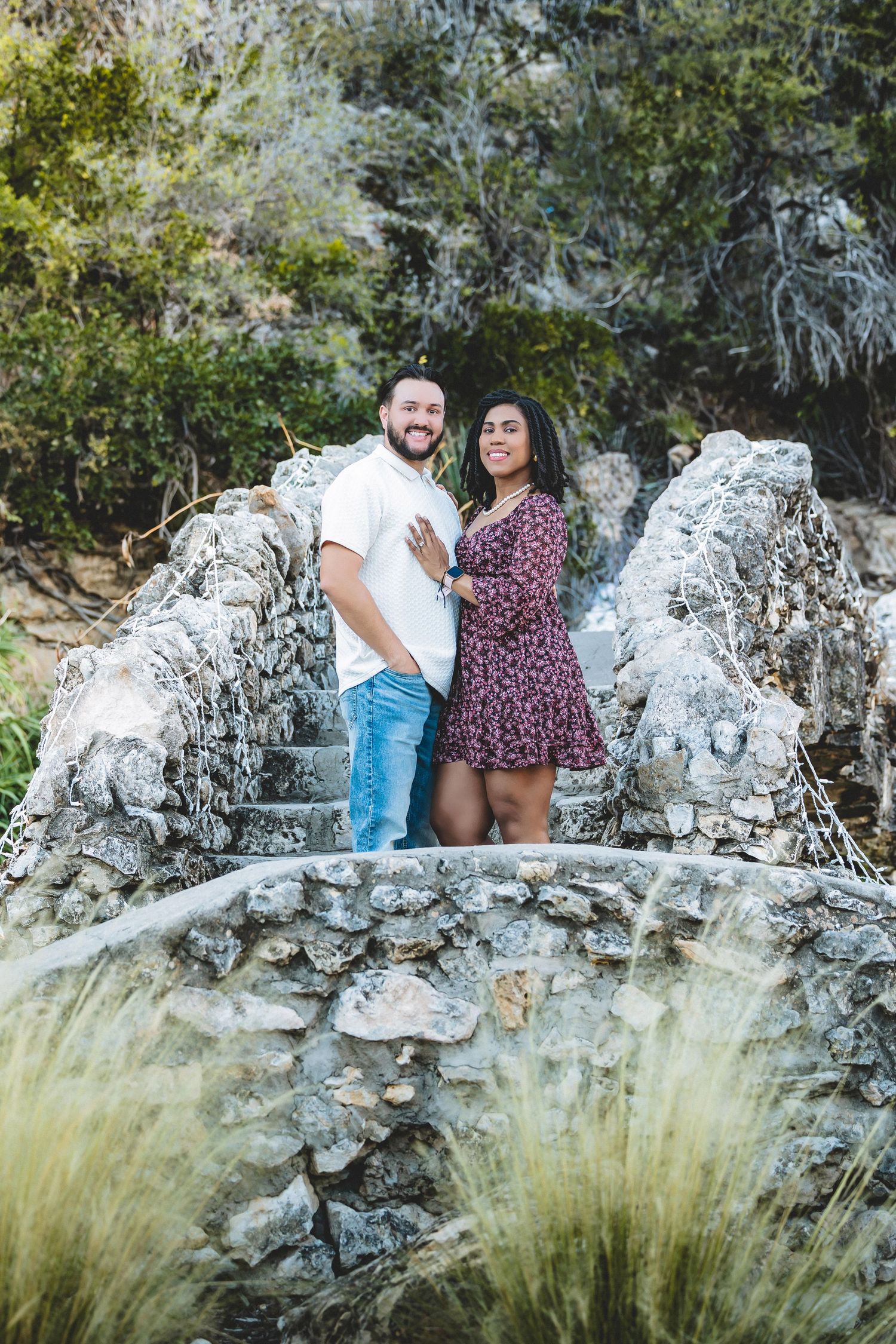 A couple sits together on white limestone rocks surrounded by natural greenery during a photo session.