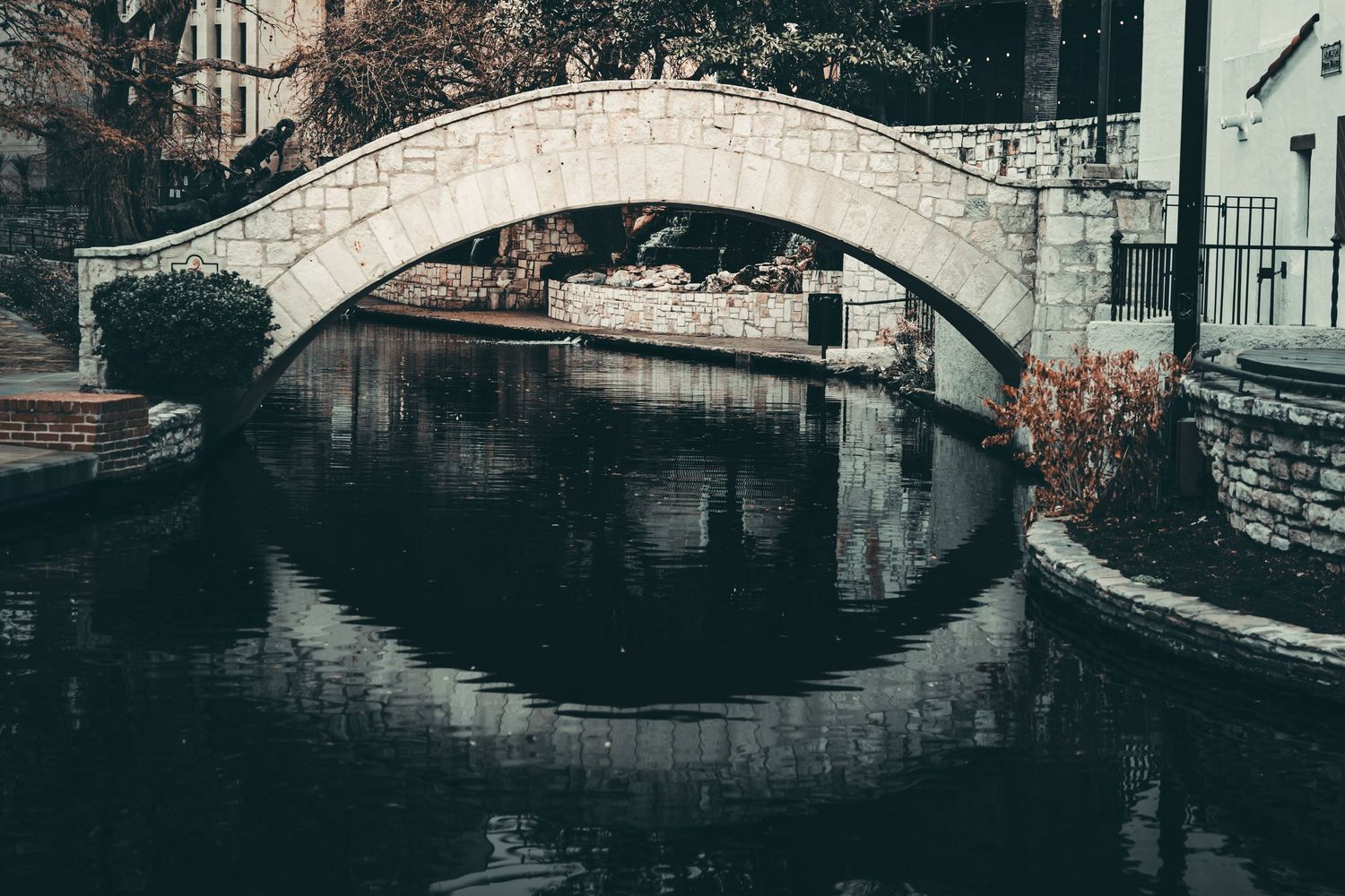 Stone arch bridge reflects in calm water creating a perfect mirror image in monochrome tones.