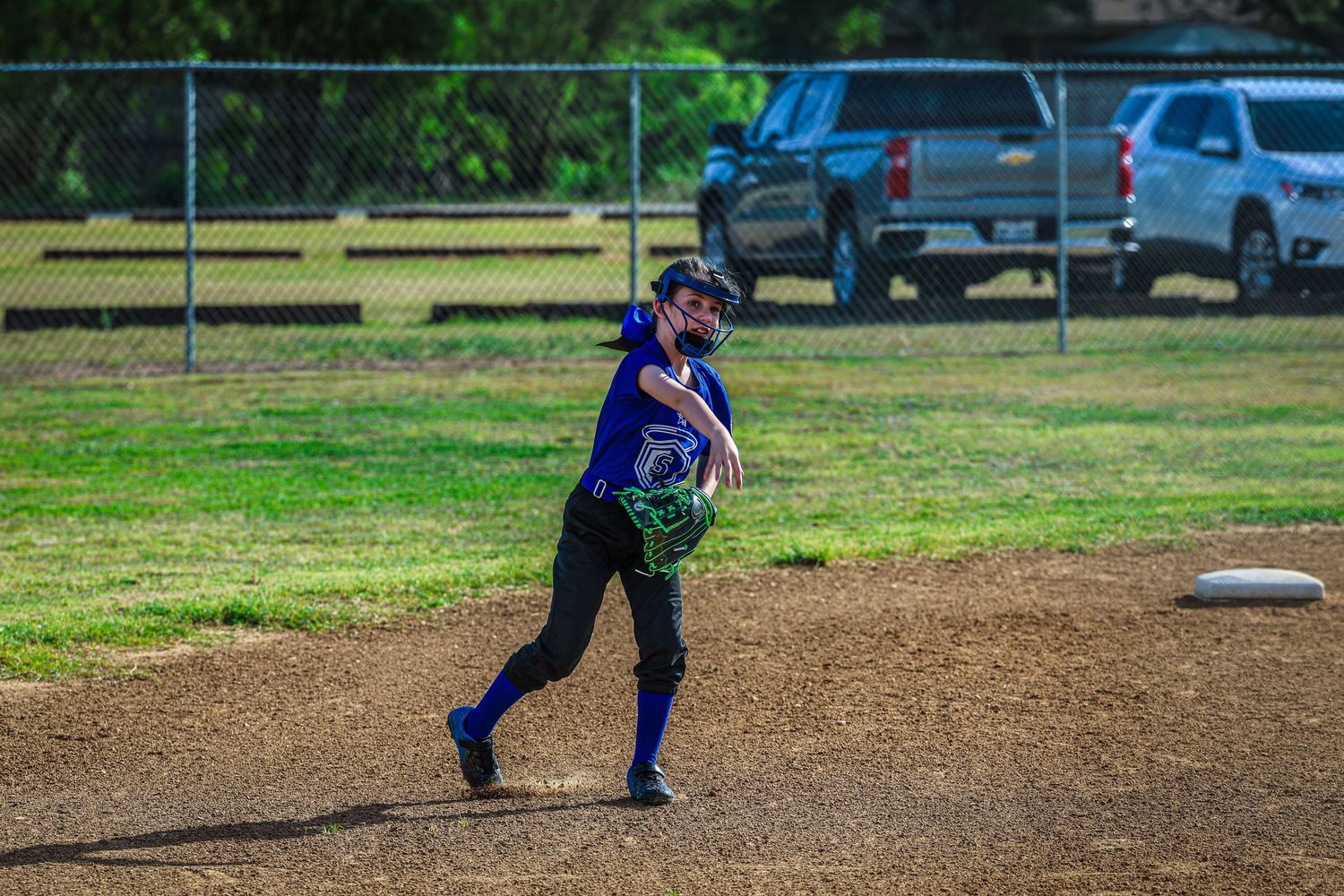 Female softball player in purple jersey winds up to throw ball during youth league game.