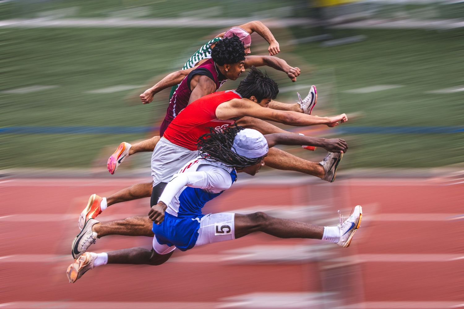 Athletes leap over hurdles in a motion-blurred track race, capturing the speed and athleticism of competitive sprinting.