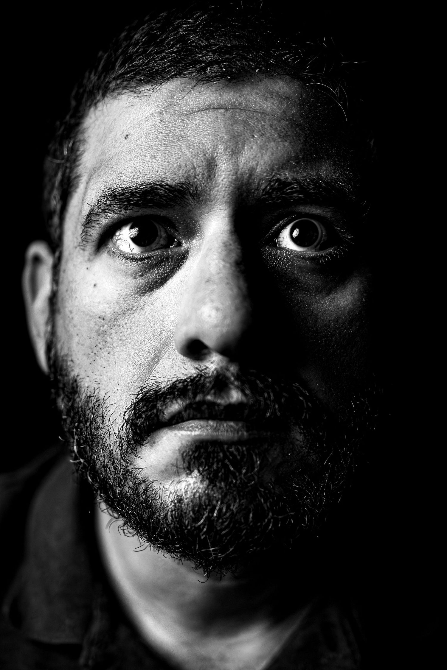 Black and white portrait of a bearded man with intense eyes against a dark background.