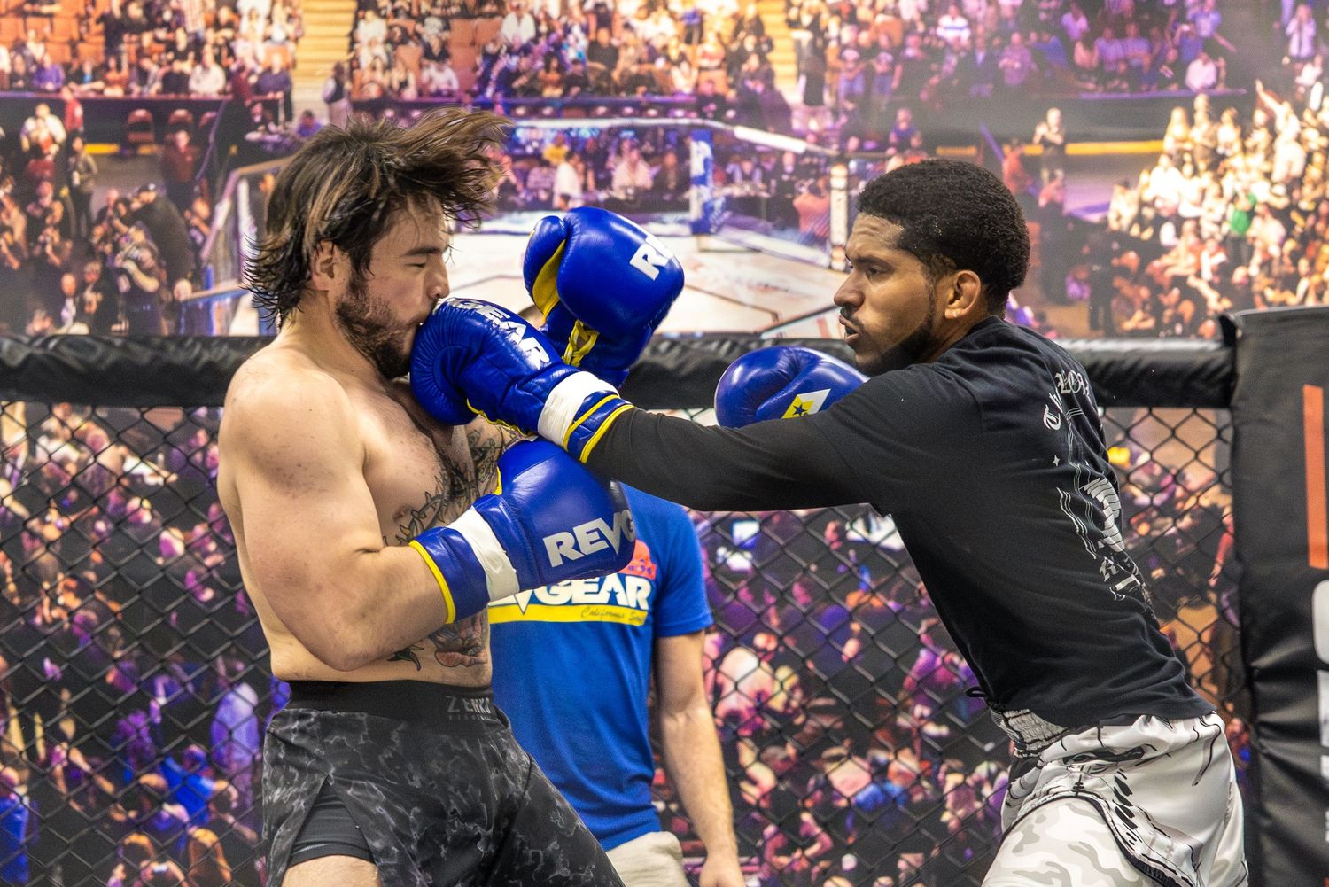 Two MMA fighters exchange punches wearing blue boxing gloves inside a cage during a professional fight event.