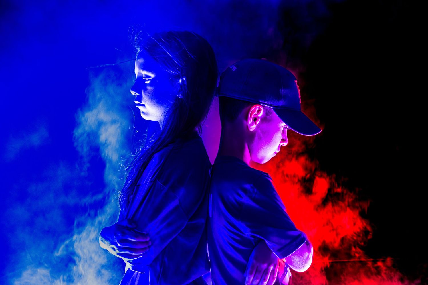 Two athletes in black stand back-to-back surrounded by blue and red smoke on dark background.