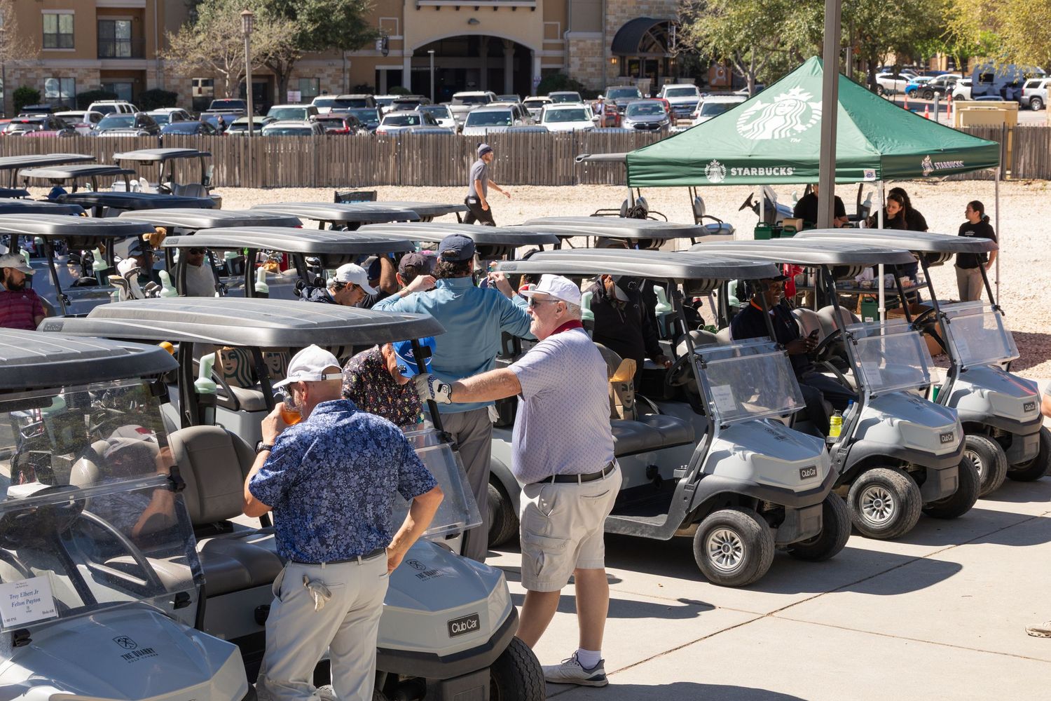 Golfers gather around golf carts at an outdoor charity tournament event on a sunny day.