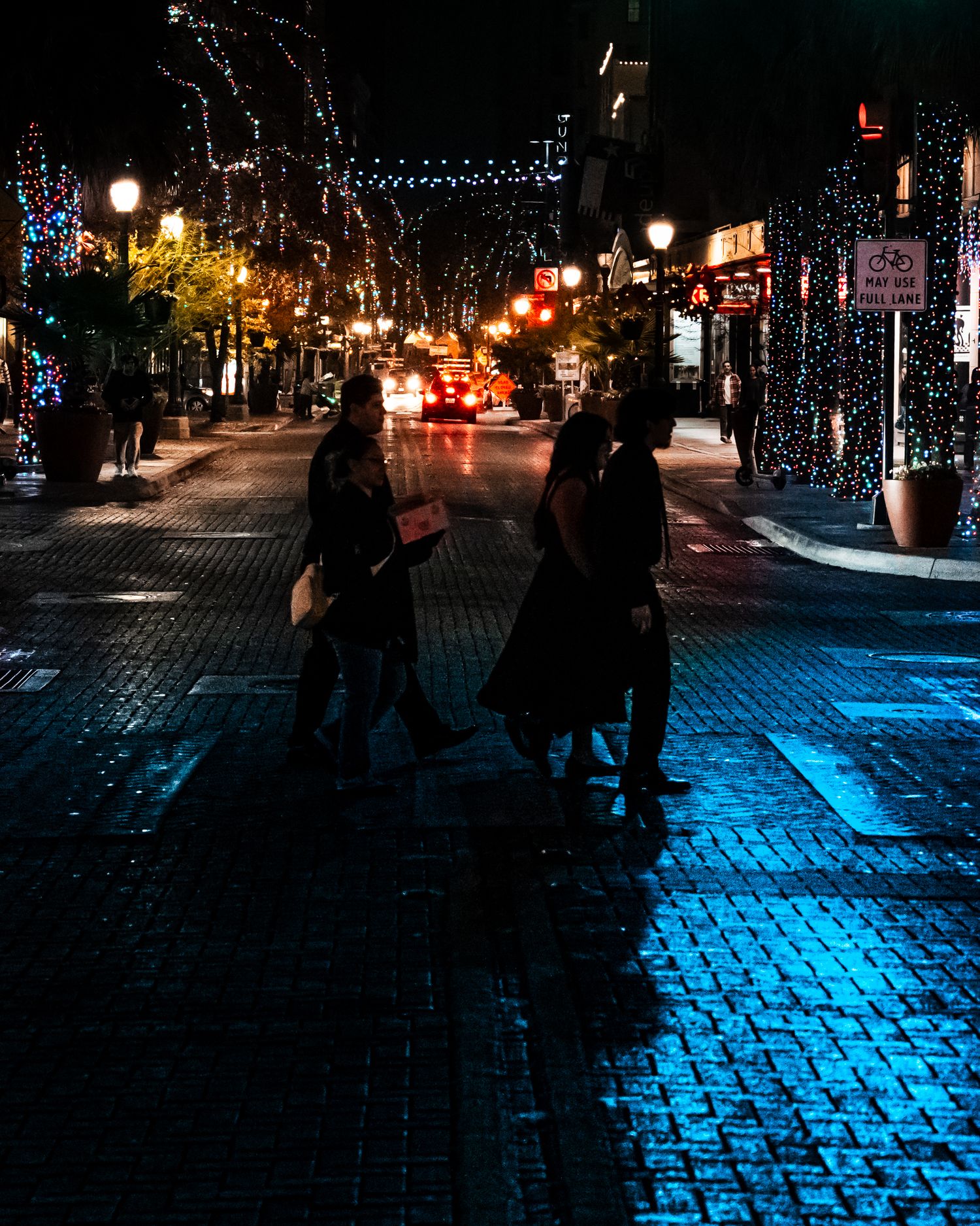 Cobblestone street at night illuminated by blue and red city lights.