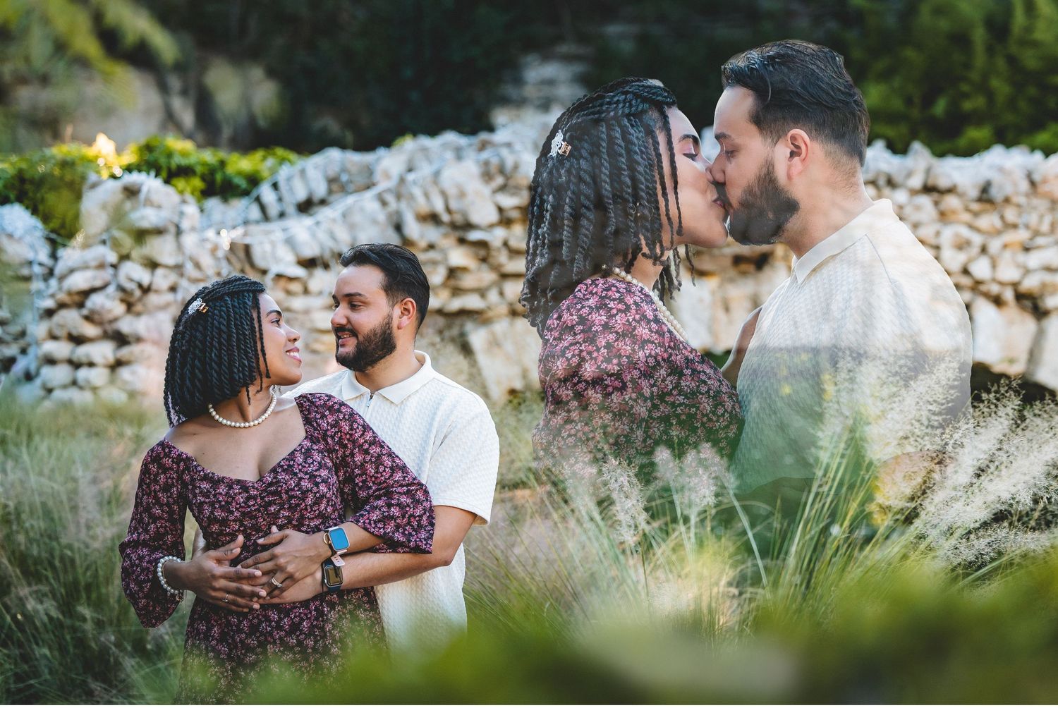 A couple embraces in a romantic outdoor setting with stone walls and natural greenery in the background.