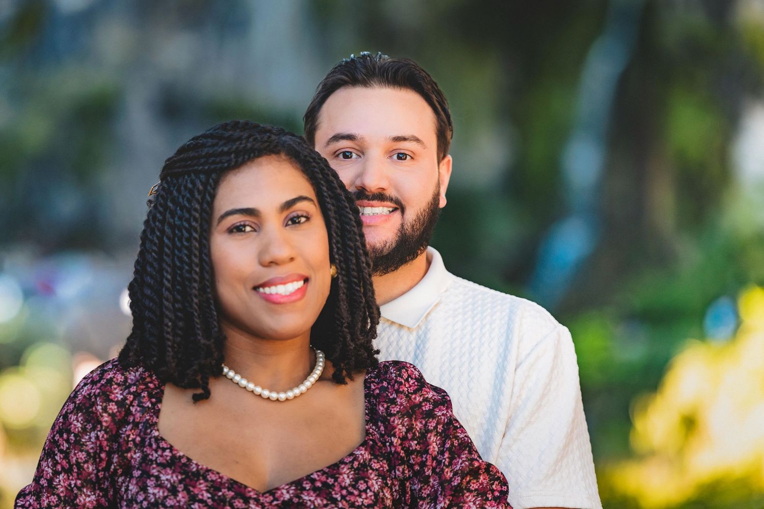 A couple poses together outdoors in a garden setting wearing coordinated burgundy and white outfits.
