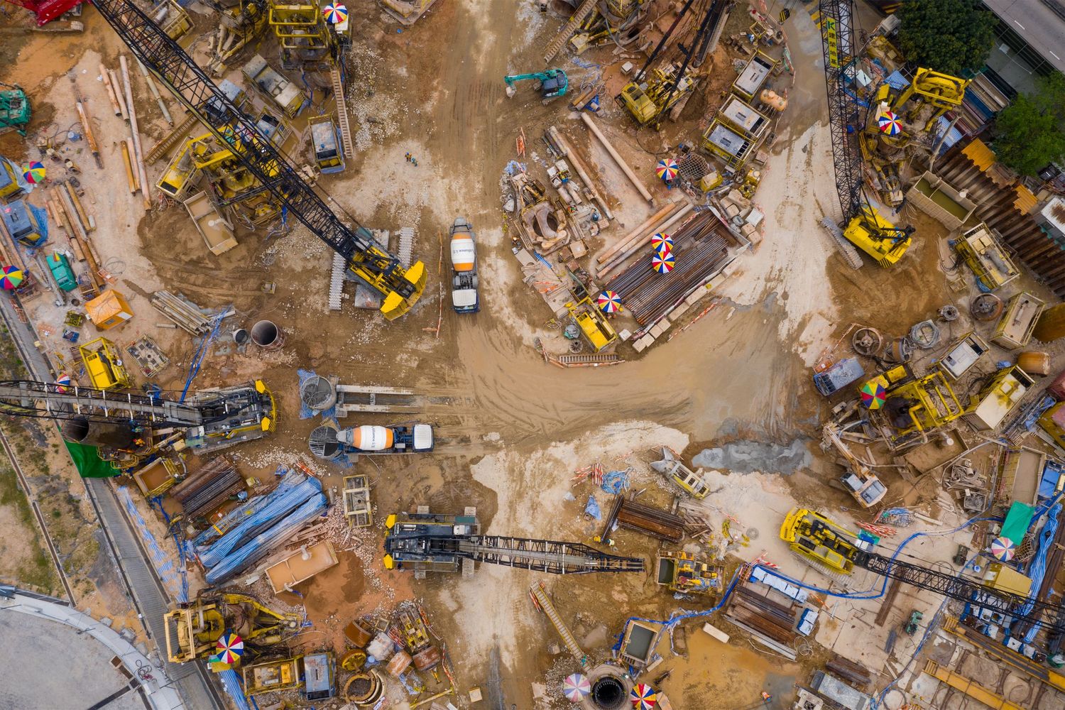 Aerial view of a busy construction site with yellow machinery, excavators, and equipment on muddy ground.