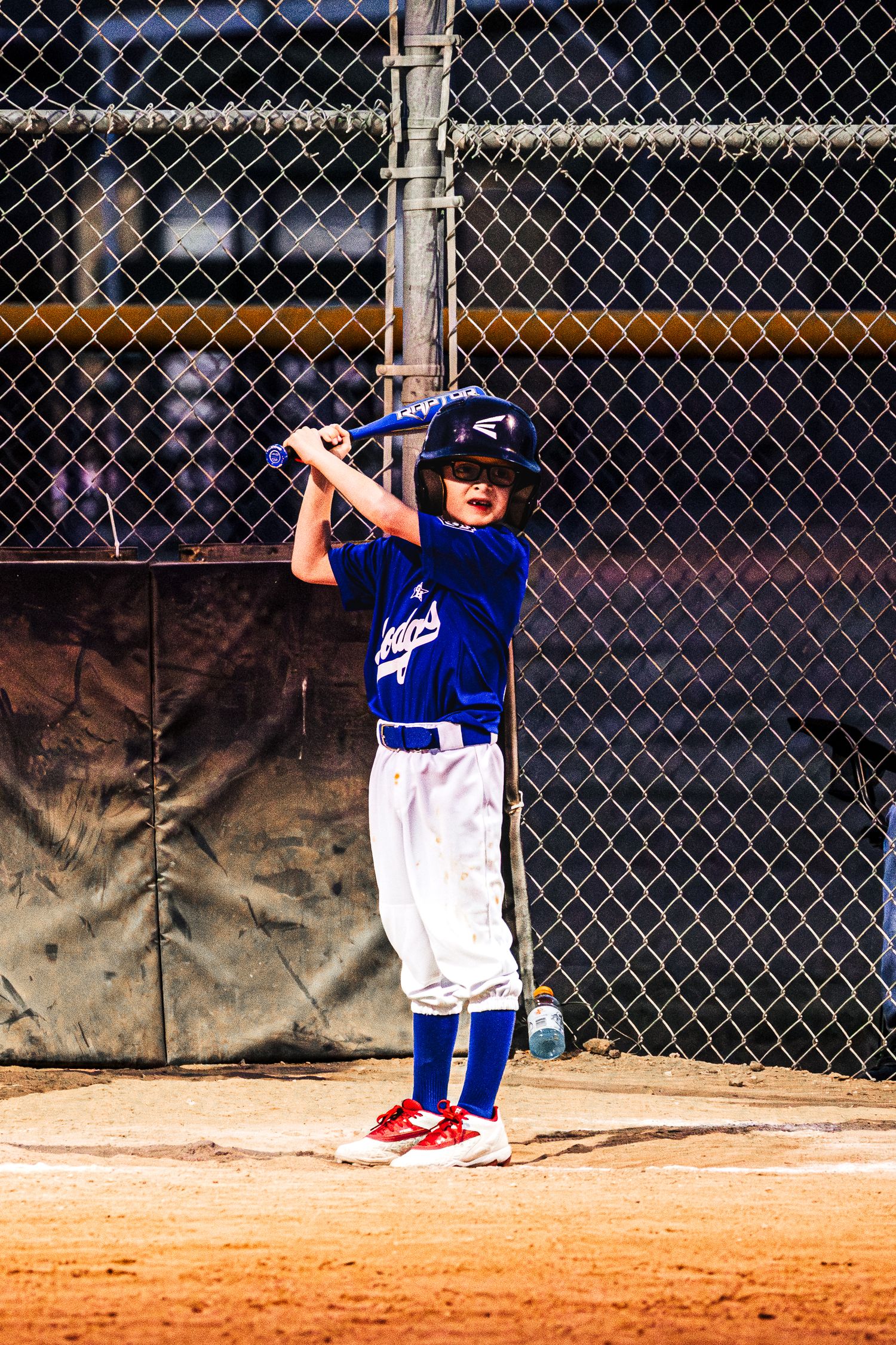 Young baseball player in blue uniform stands ready to bat at home plate during a little league game.