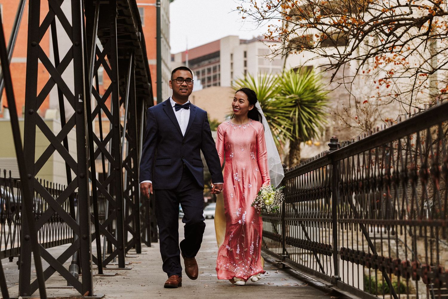 A couple walks along a wrought iron railing pathway outside a historic stone building.