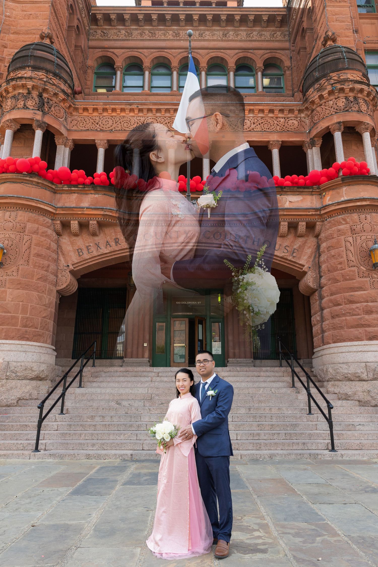 A couple poses for wedding photos in front of a historic red brick courthouse building with stone steps.