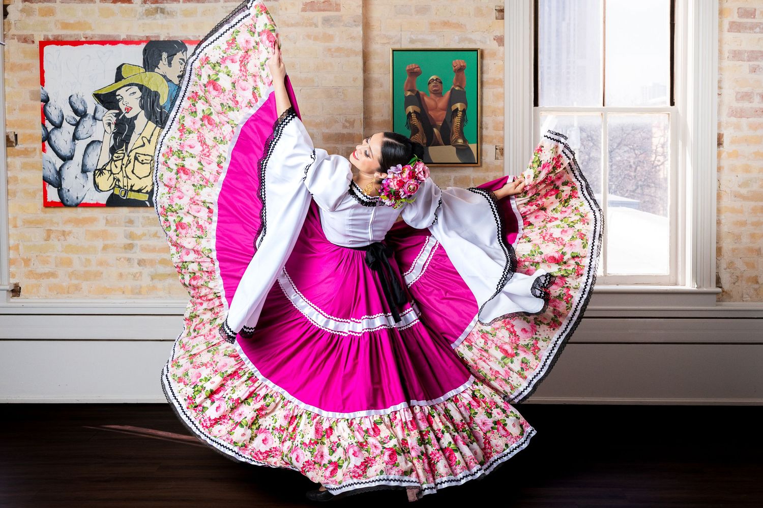 A bright pink skirt with floral pattern twirls outward in a circular motion against a brick wall background.