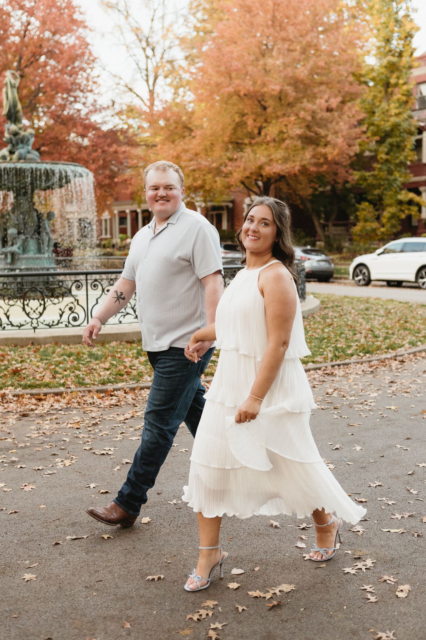 A couple dances playfully among scattered fall leaves on a paved walkway.