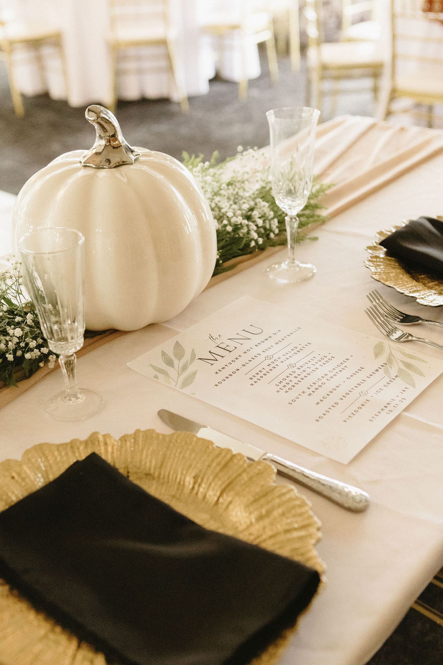 Elegant wedding reception table setting with white pumpkin decor, menu cards, and gold charger plates.