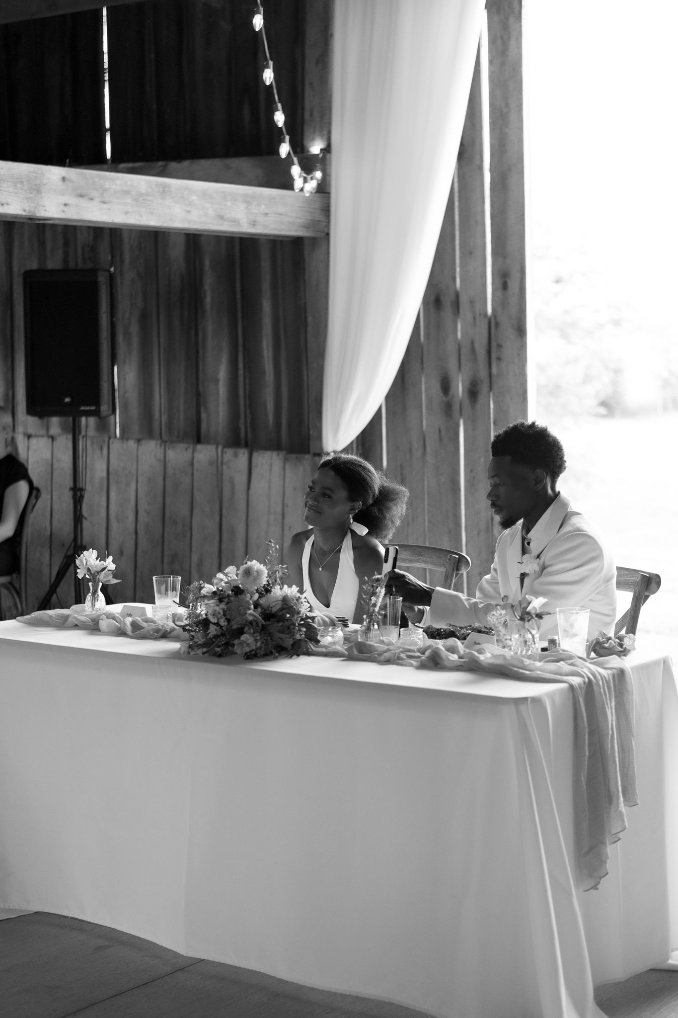 Black and white shot of a decorated reception area with banquet tables and white tablecloths in a rustic venue.