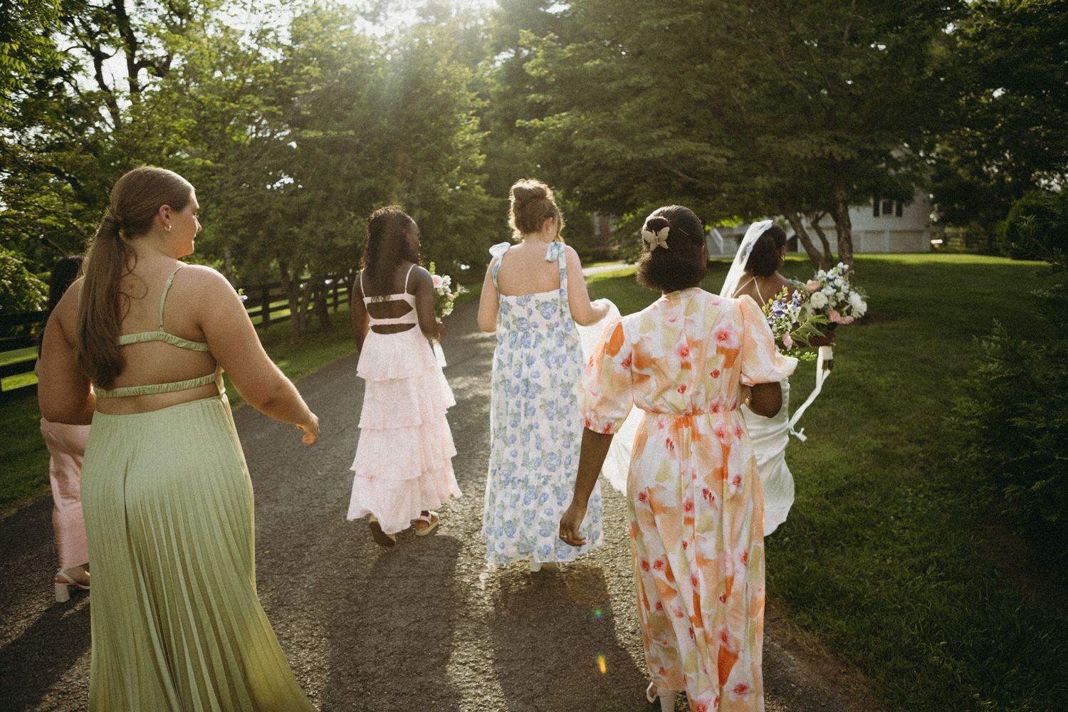 Wedding party members walk together on a garden path during golden hour.