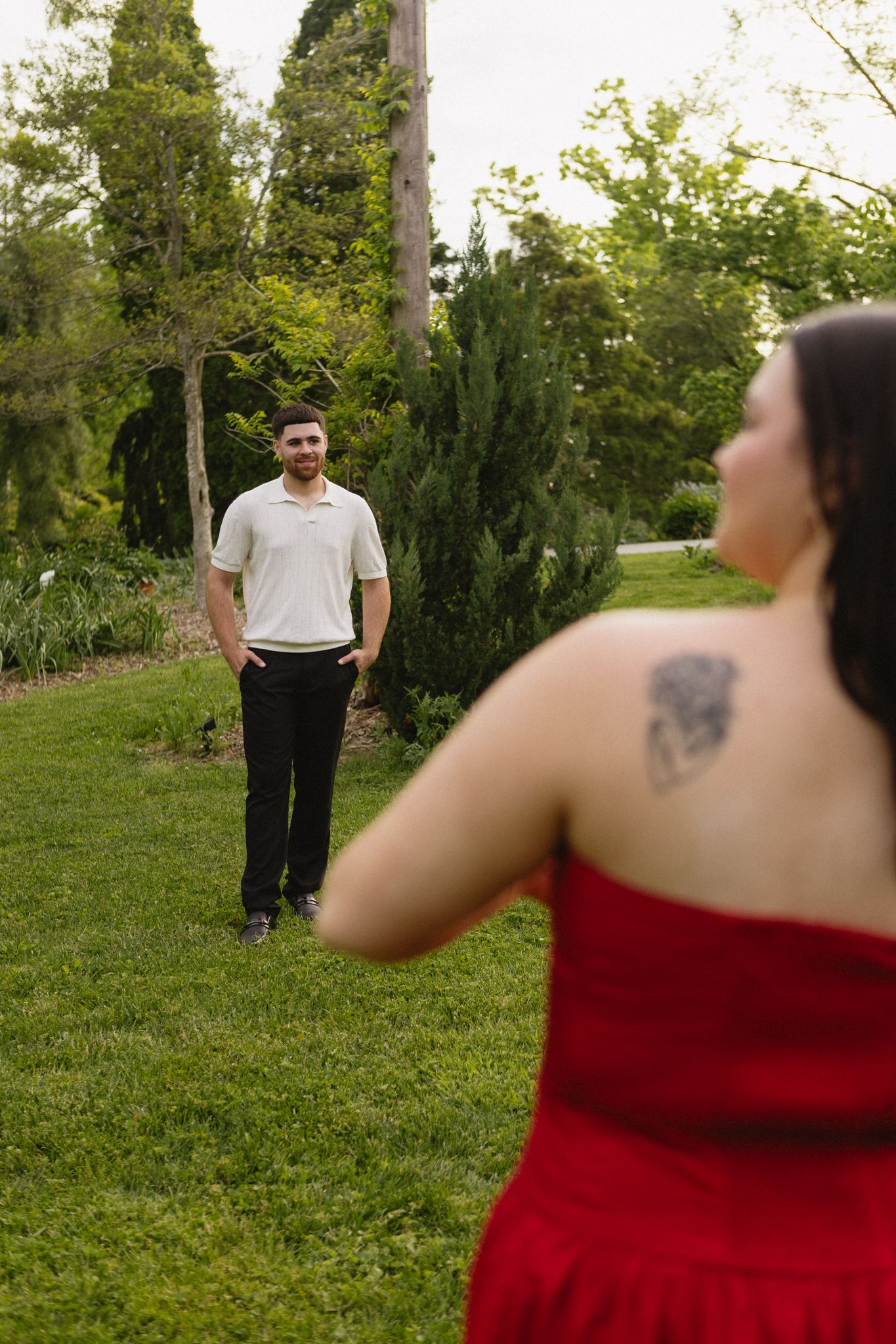 A romantic outdoor photoshoot with two people in a garden with tall evergreen trees.