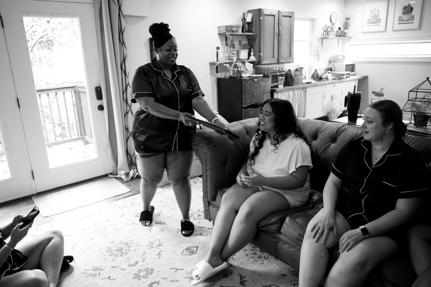 People gather in conversation on a couch in a casual living room setting captured in black and white photography.