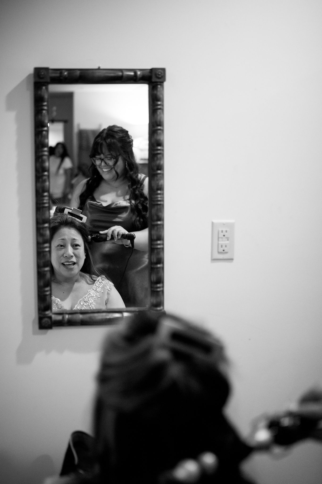 Black and white reflection in mirror shows preparation scene with beauty styling taking place.