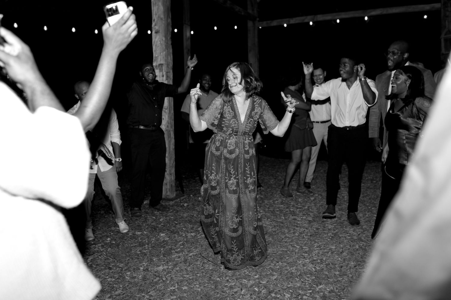 A group of people dancing and celebrating at night under string lights at an outdoor party.