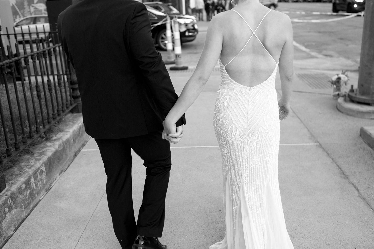 Back view of a couple walking, showcasing the bride's elegant backless lace wedding gown.