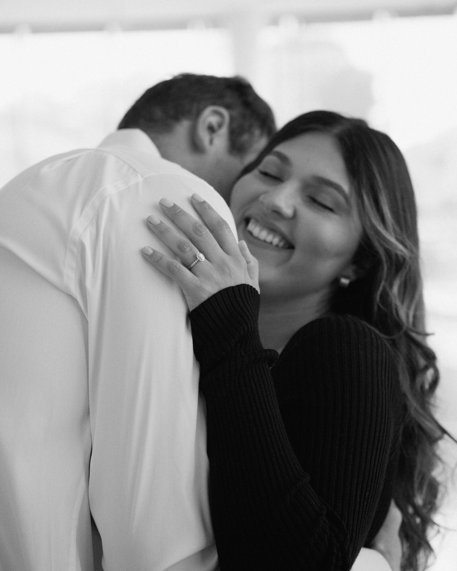 Elegant engaged couple smiling and embracing in downtown Louisville, with the woman showing her engagement ring