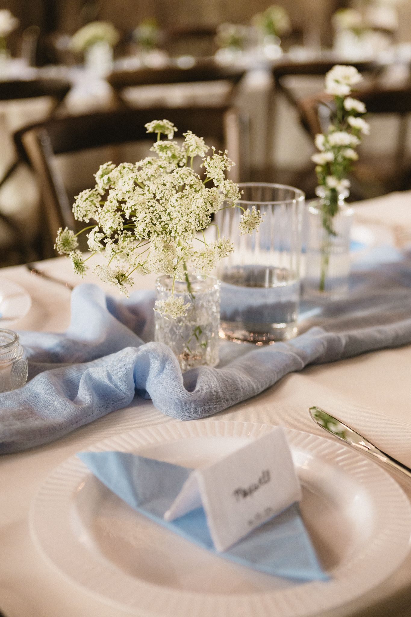 Elegant table settings with light blue napkins and delicate baby's breath flowers in small vases on white plates.