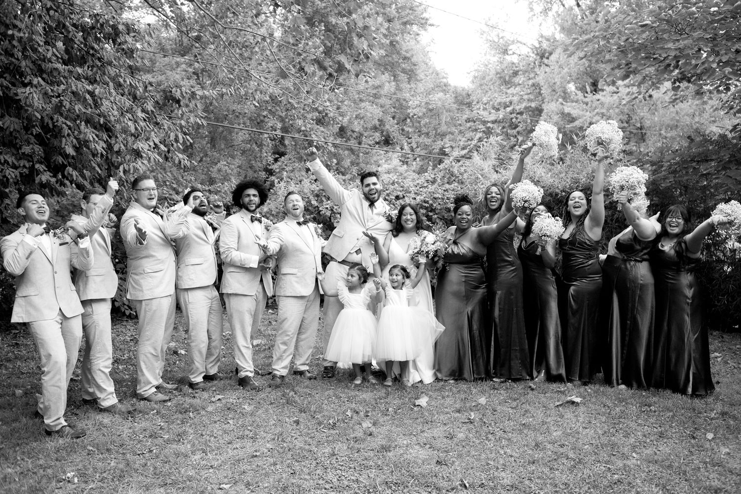A wedding party in black and white photography poses together on a lawn with bridesmaids in contrasting light and dark dresses.