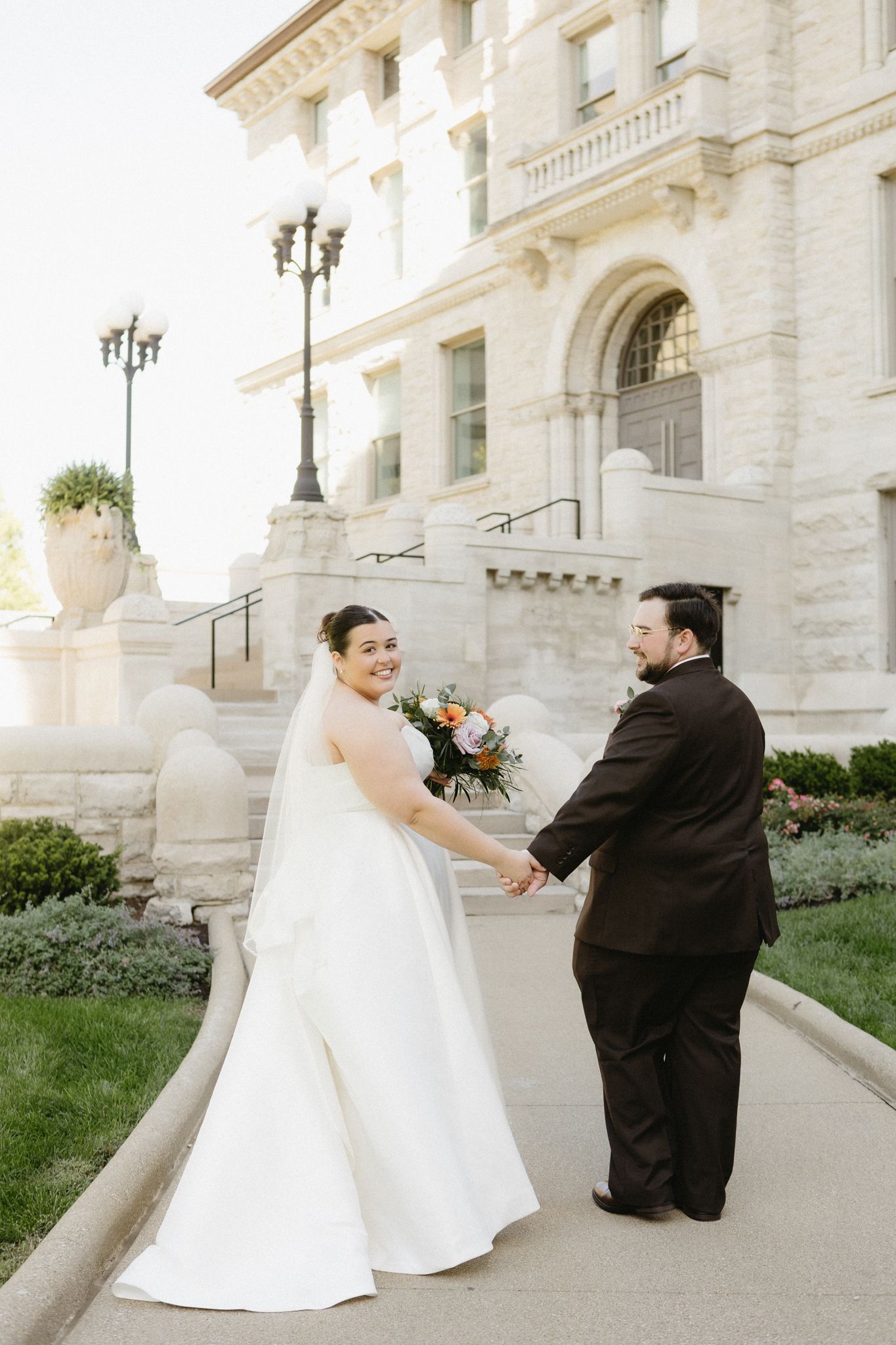 A wedding couple poses for romantic photos in front of a grand white stone building with classical architecture.
