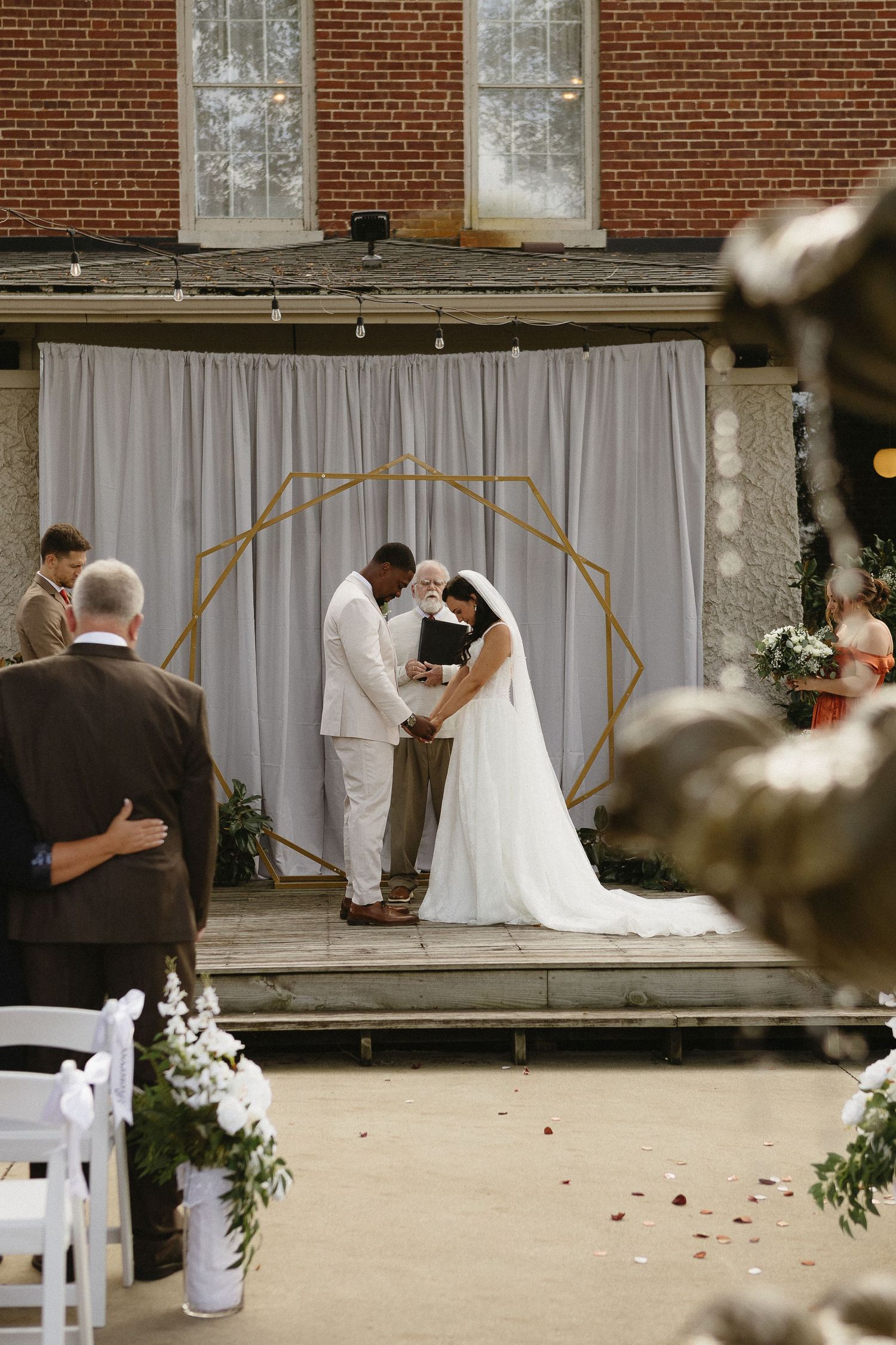 Outdoor wedding ceremony setup with white chairs and arch against a brick building backdrop.