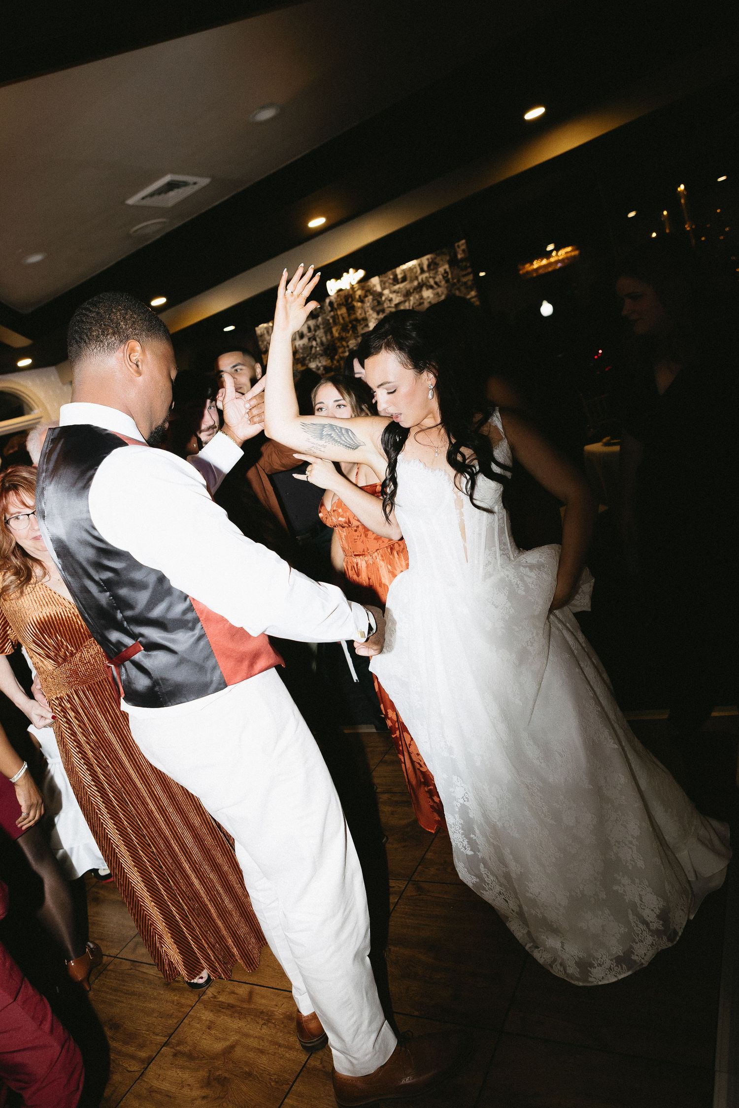 Wedding guests dancing energetically on a dark dance floor at a reception.