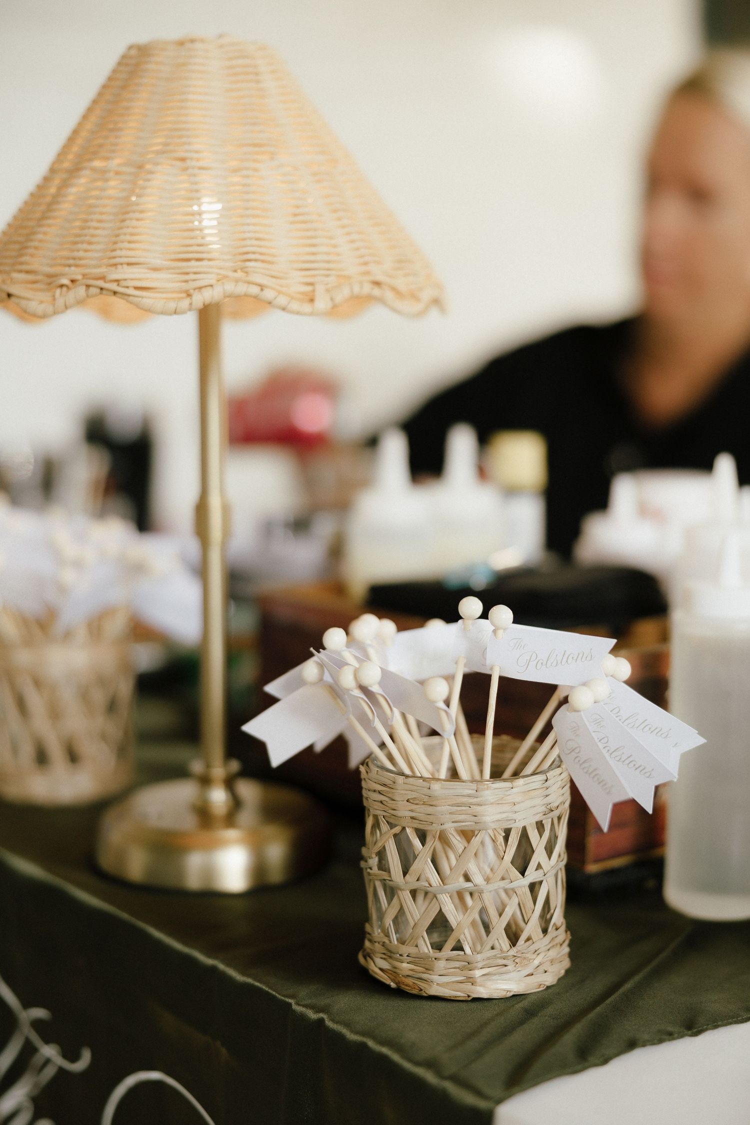 Wicker lamp and decorative holder with white ribbon sticks on a green table at an elegant event.