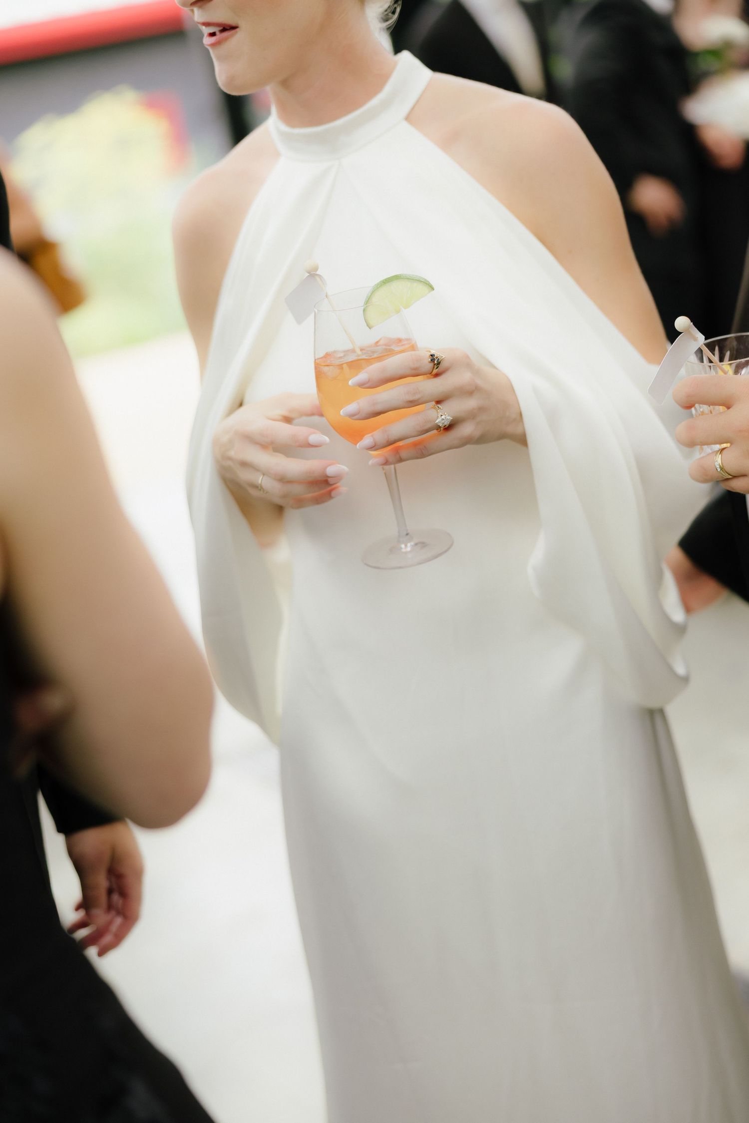 Bride in white halter gown holding an orange cocktail garnished with lime at a wedding reception.