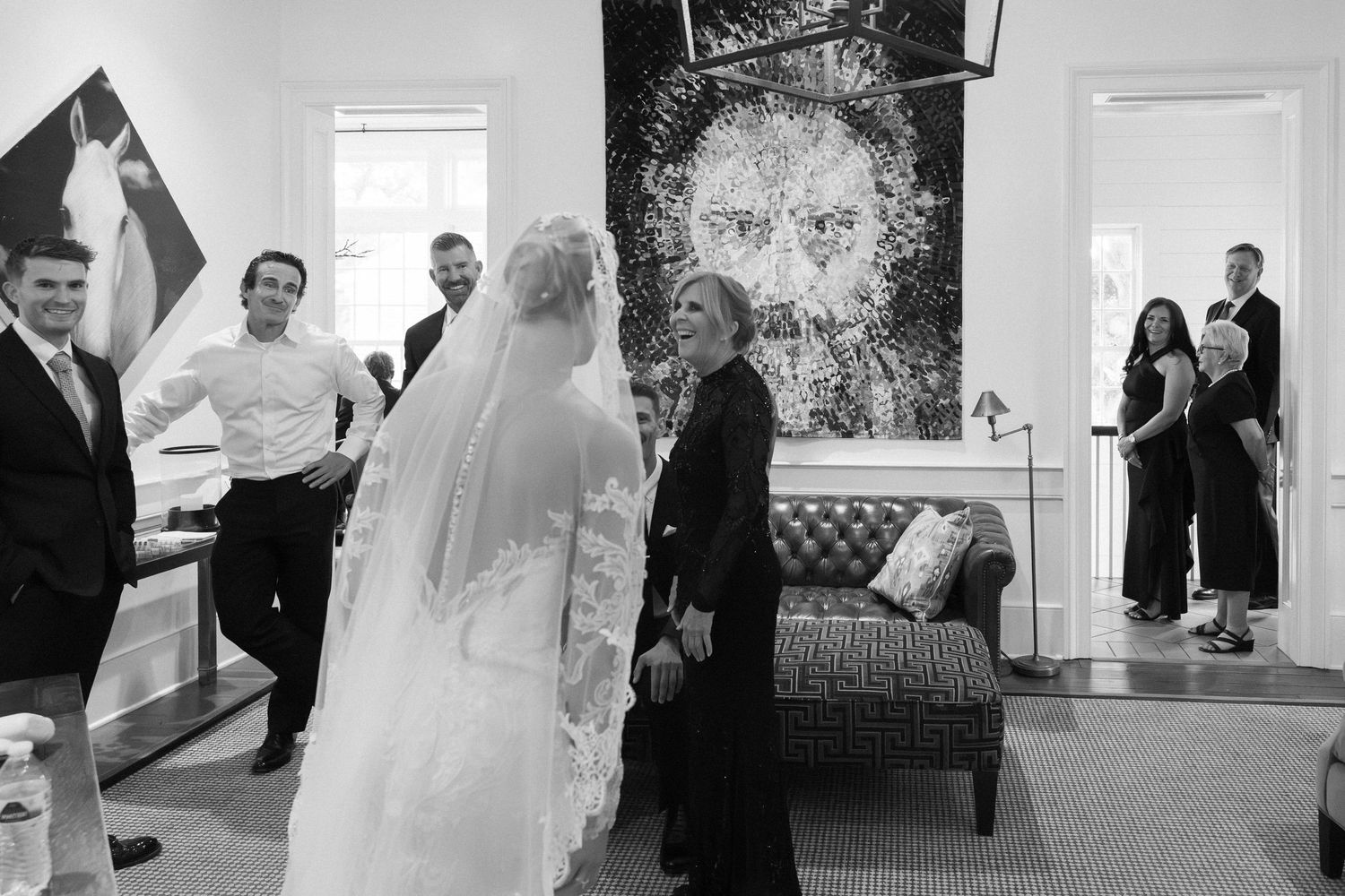 Black and white wedding photo of bride in lace gown and veil with wedding party in elegant venue with portrait art.