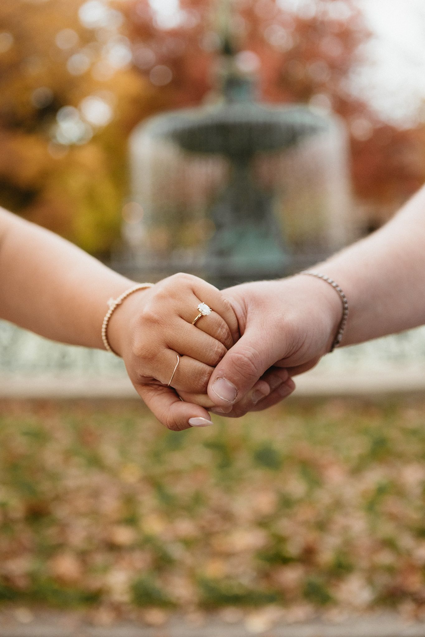 Two hands reaching towards each other with rings against a blurred autumn background with fallen leaves.