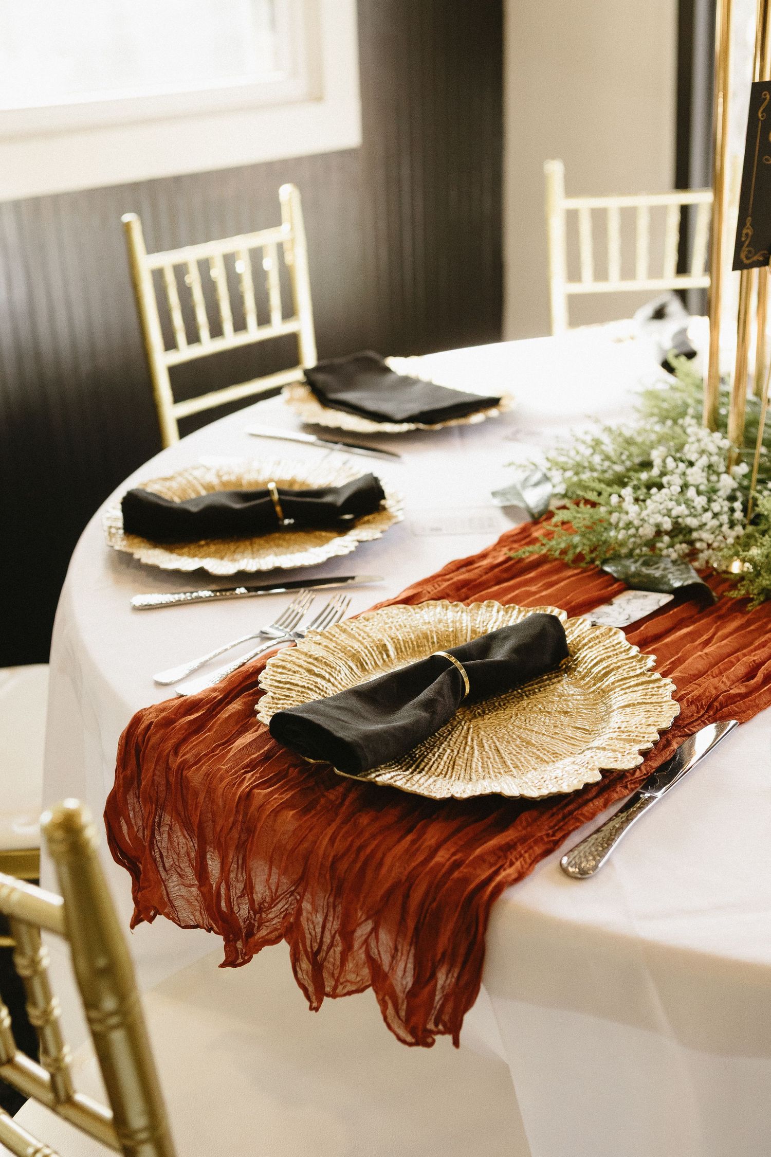 Wedding table settings with burgundy runners and gold shell-shaped charger plates.