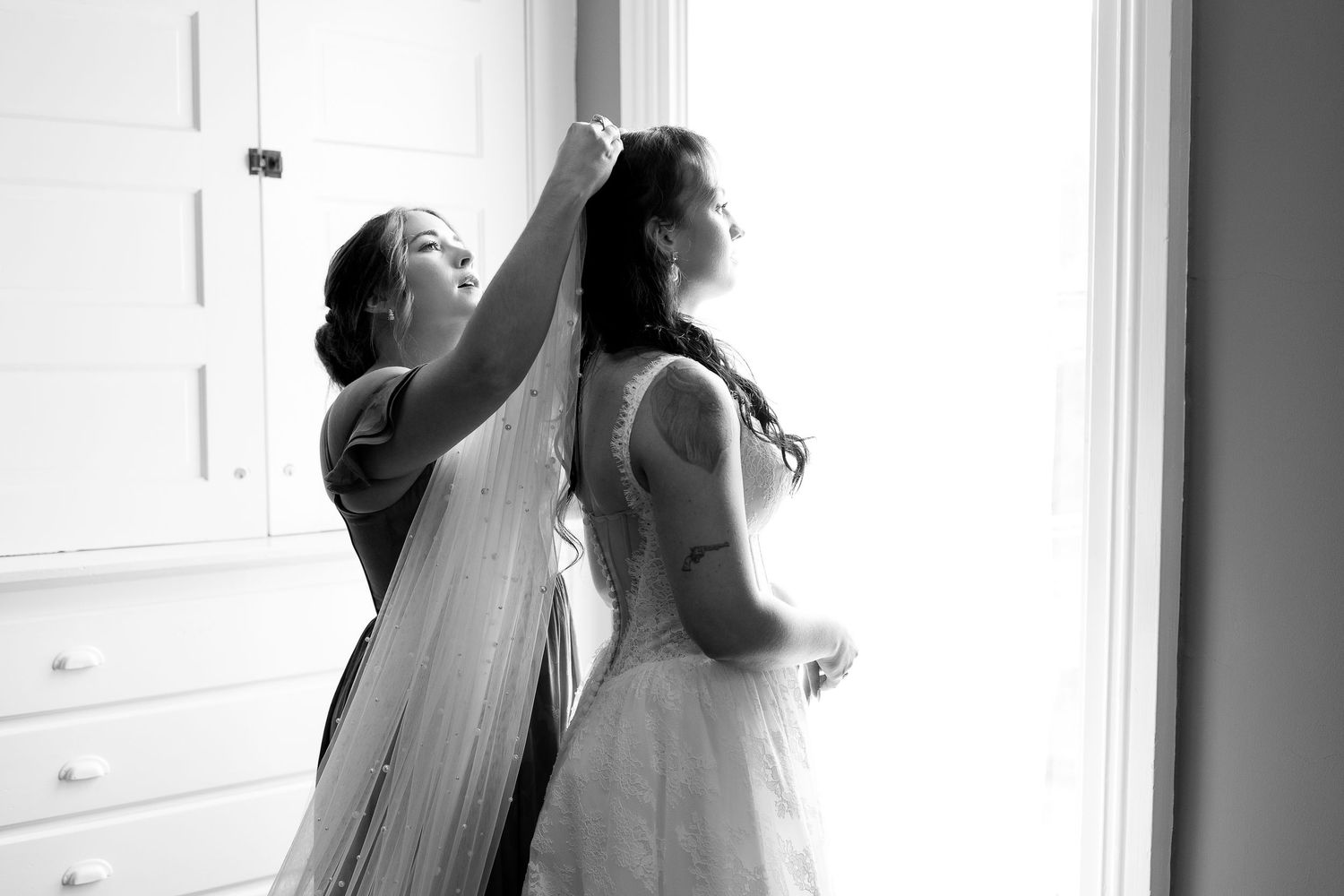 Bridesmaids in burgundy dresses getting ready in a sunlit room.