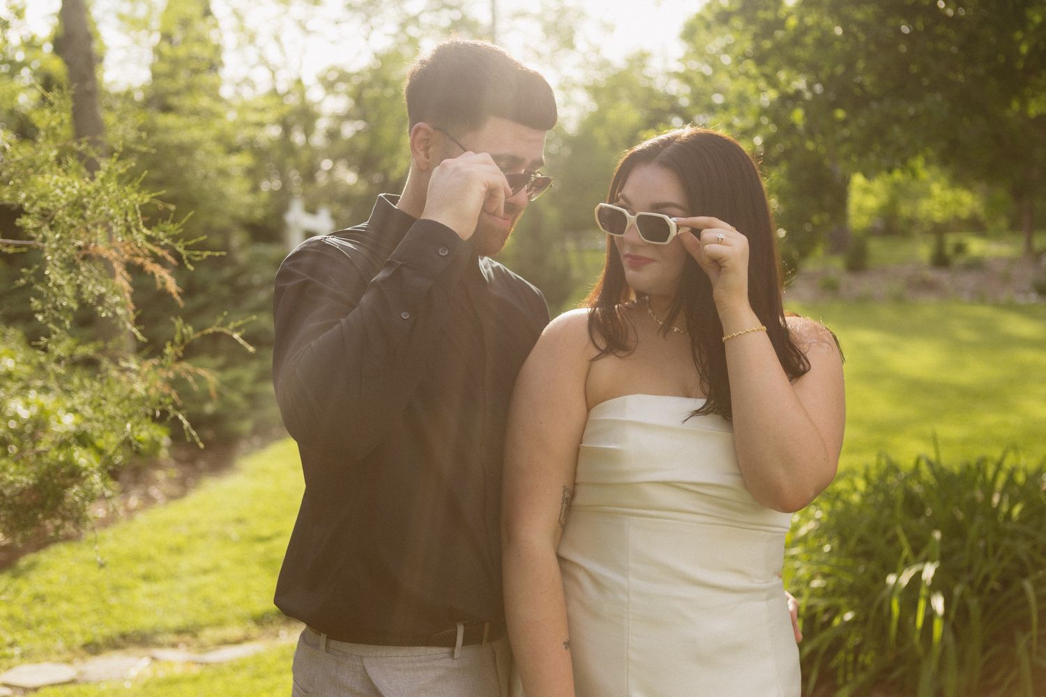 Romantic couple lounging on a striped picnic blanket in a lush green garden setting bathed in warm sunlight.