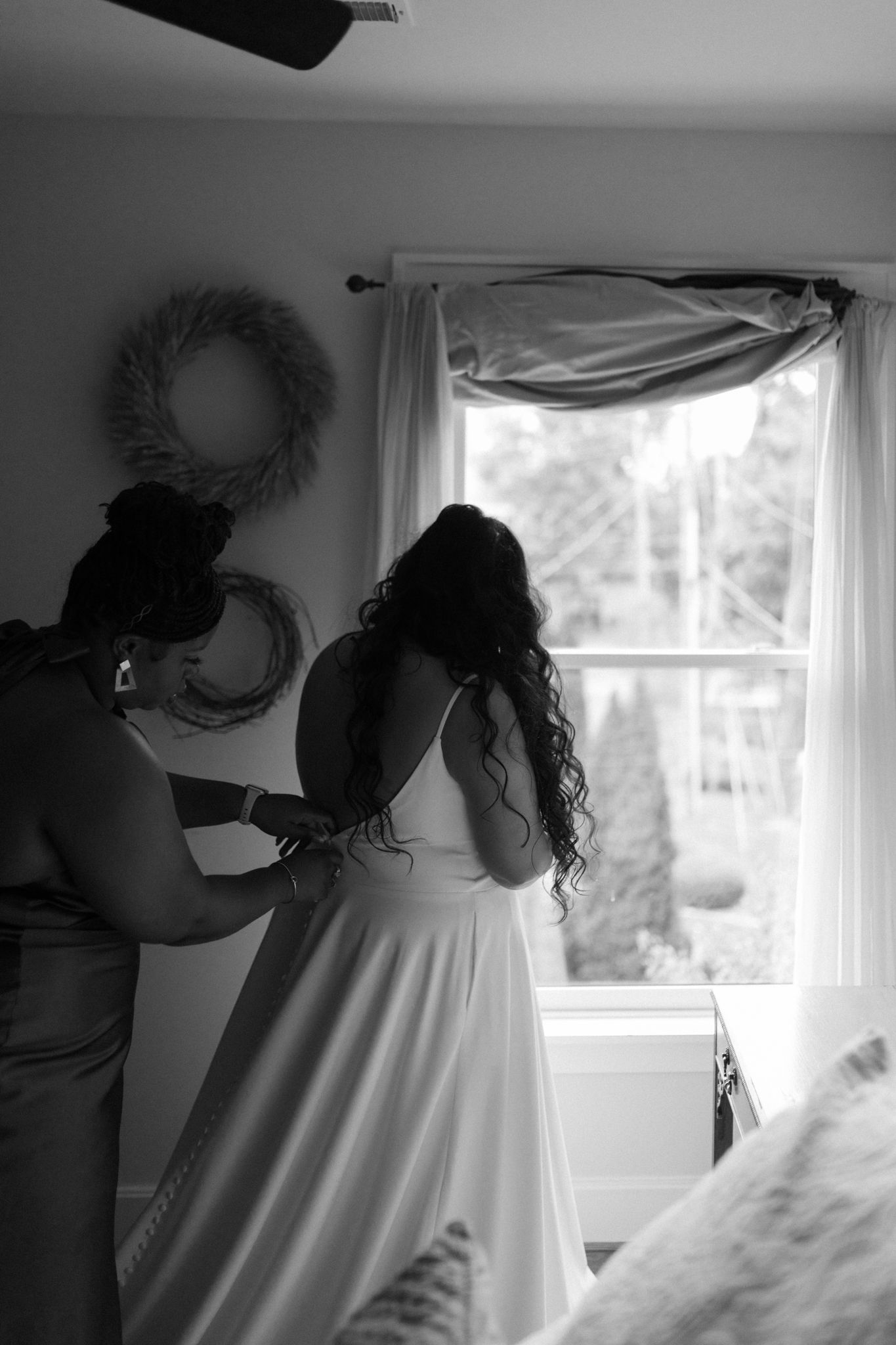 Wedding preparation scene with dress adjustment by window in black and white.