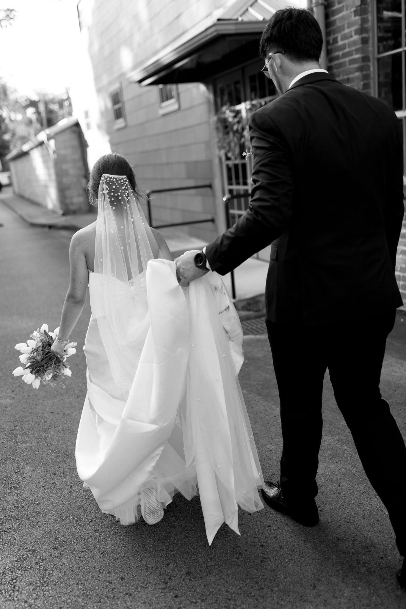 bride and groom walking together, groom helps bride with dress by holding it