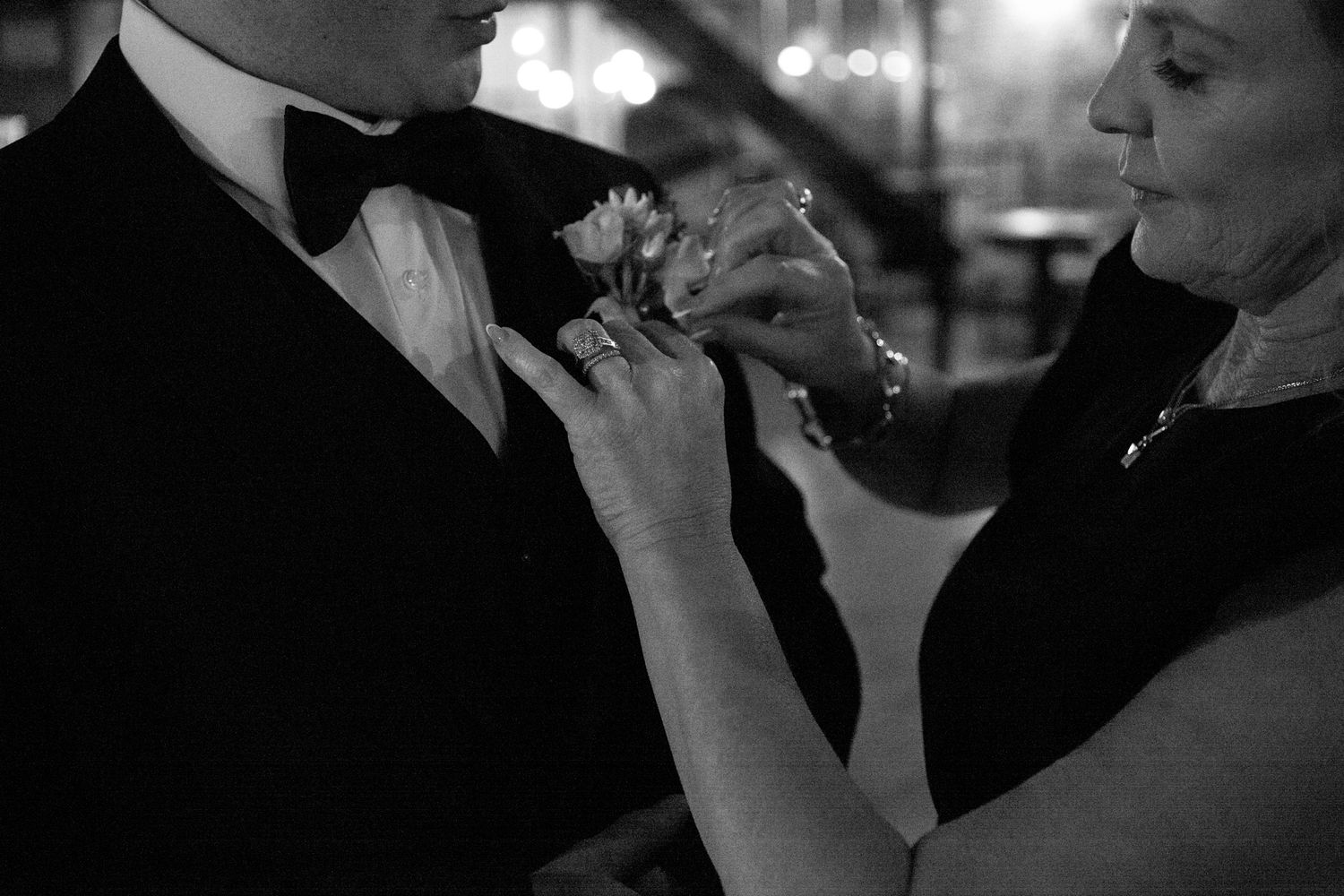 A close-up shot of a boutonniere being pinned onto formal attire in black and white.