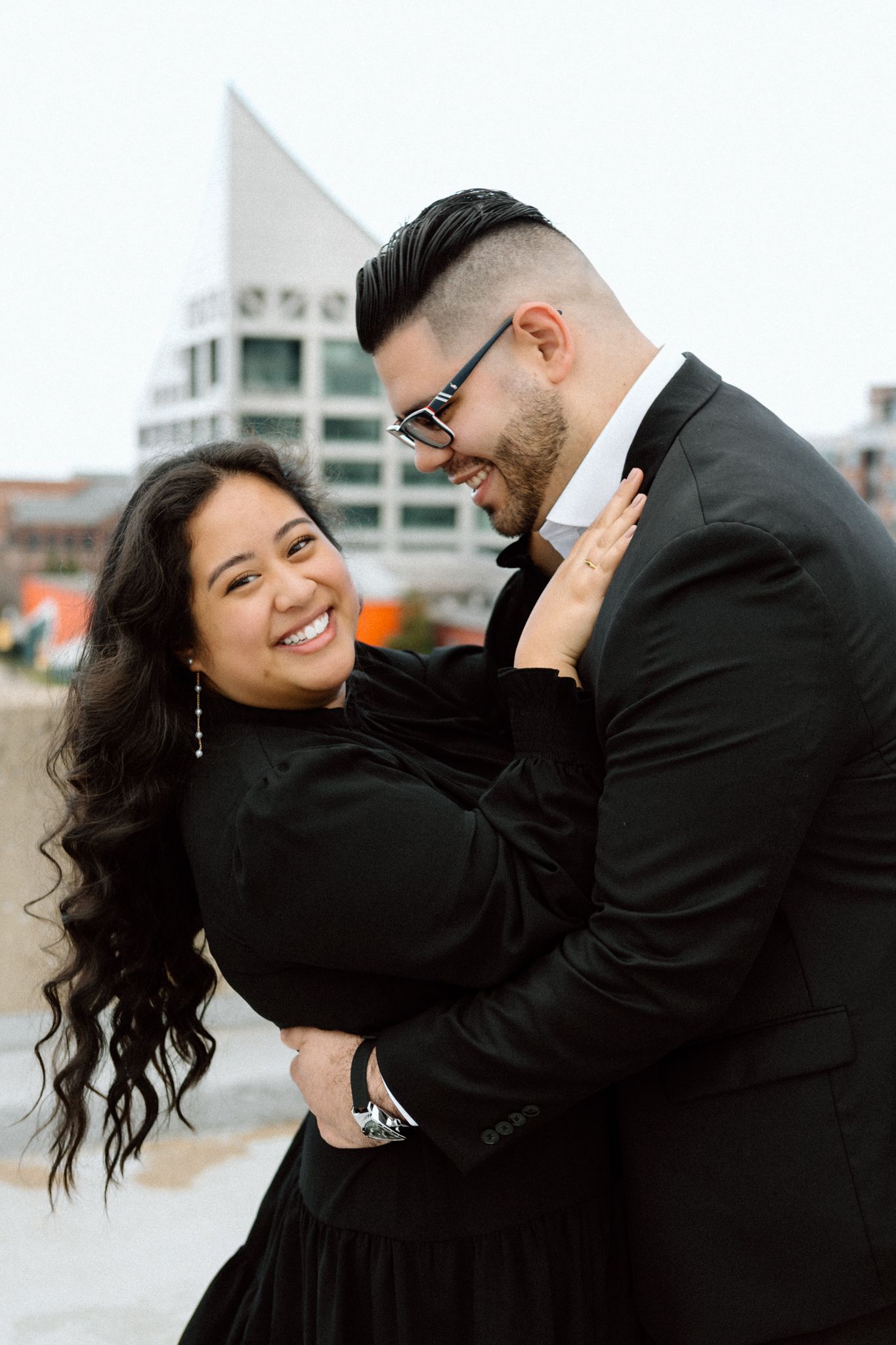 Elegant engaged couple smiling and embracing in downtown Louisville, with the woman showing her engagement ring
