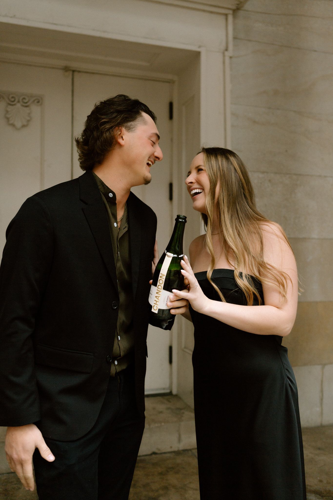 Engaged couple celebrating with a bottle of Chandon, sharing a joyful moment and laughter in downtown Louisville