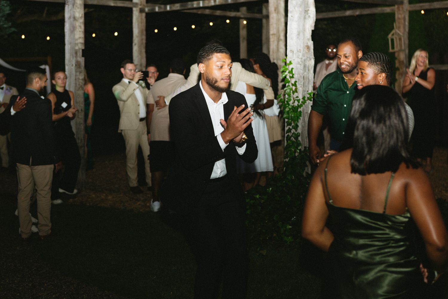 A group of people dancing and celebrating at night under string lights at an outdoor party.