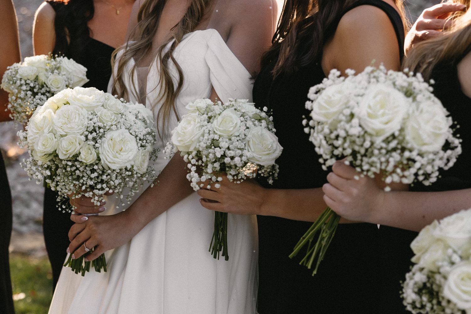 Row of bridesmaids holding elegant white rose and baby's breath bouquets at a wedding ceremony.