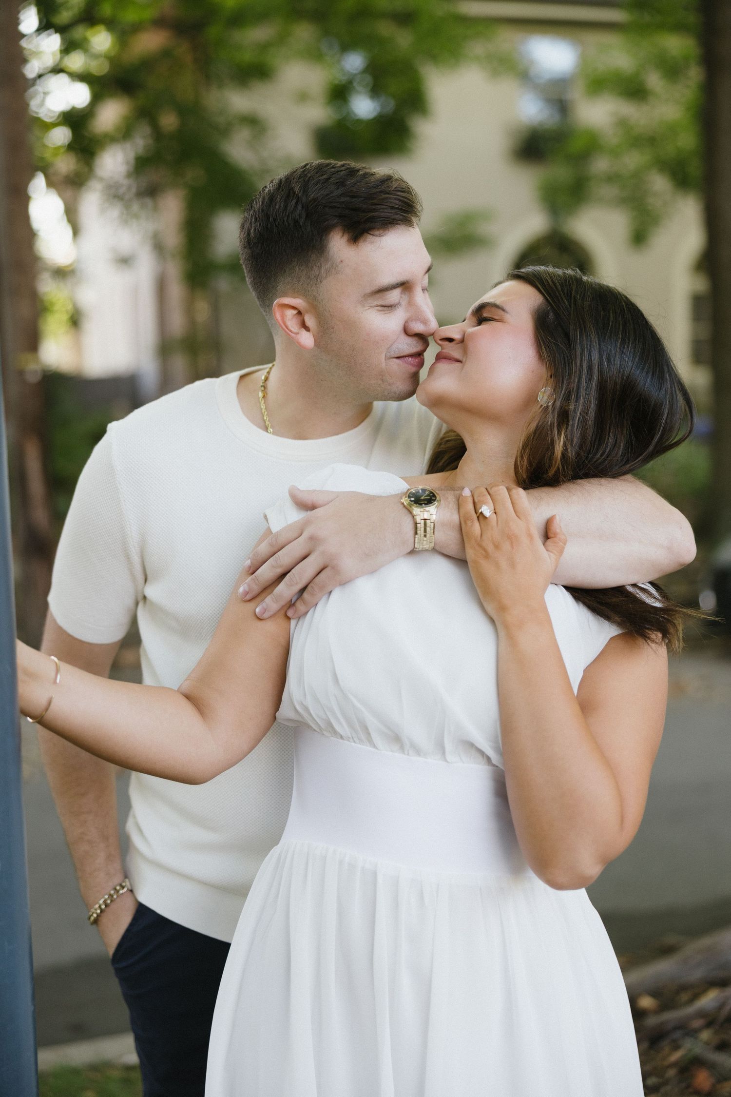 Romantic couple about to kiss outdoors, man in white shirt and woman in white dress exchanging tender moment.