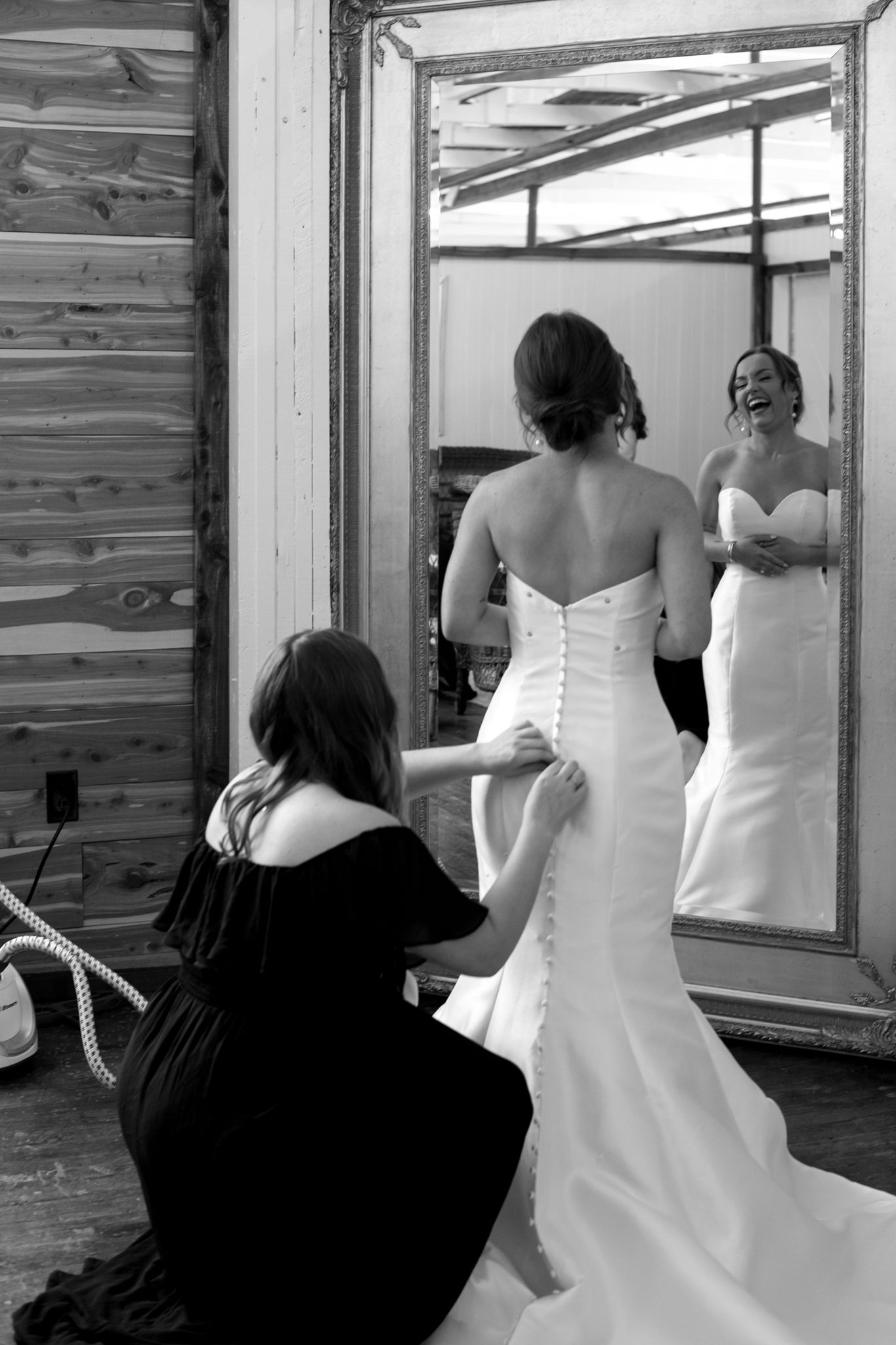 A woman lovingly helps a bride into her wedding dress, symbolizing friendship and the beauty of shared moments before th