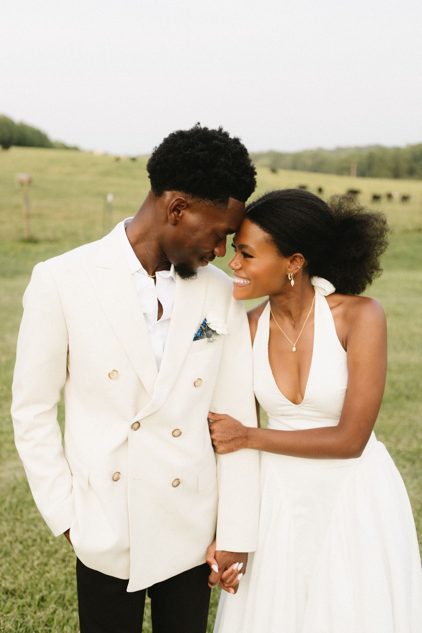 Romantic couple in elegant white wedding attire share intimate moments against a scenic rural backdrop.